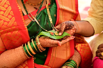 hands holding golden mangalsutra on leaf. Wedding indian jewelery. Bride and groom hands in...