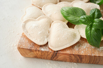 Italian ravioli pasta in heart shape. Tasty raw ravioli with flour and basil on white background. Food cooking ingredients background. Valentines or Mothers Day lunch ideas. Top view with copy space.