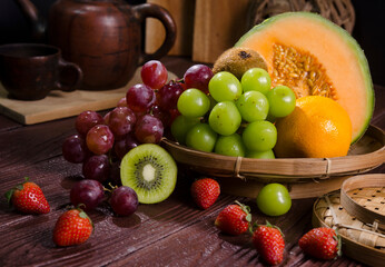 tropical fruits such as grapes, orange, melon, kiwi and strawberries are served on a wooden table.