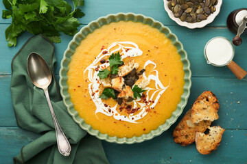 Pumpkin and carrot cream soup with herbs, seasonings and seeds in bowl on dark wooden background in rustic style. Thanksgiving traditional autumn pumpkin cream soup. Top view.