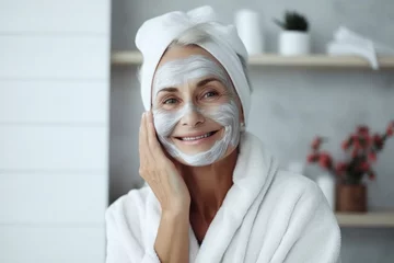 Crédence de cuisine en verre imprimé Spa A beautiful elderly gray-haired woman with a cosmetic nourishing moisturizing mask on her face smiles on gray background. Facial skin care concept, beauty, care, cosmetology