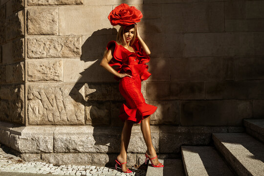 Glamour, elegant woman woman stylized as a rose flower is wearing red Ruffle dress and is posing outdoor on a summer day.