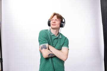young handsome red-haired man in a green t-shirt enjoys and gets high from listening to music in headphones