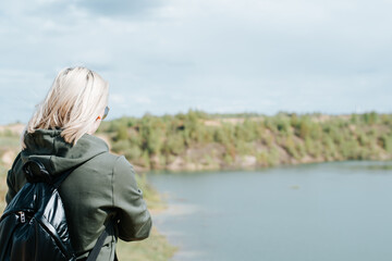 Fototapeta premium Back view of a lonely woman in casual clothes on the shore of a lake, copy space