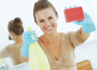 Happy young housewife showing spray bottle and sponge