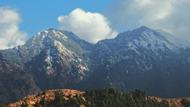 Time-lapse of the Himalayan snow-capped mountains during sunset with moving clouds and blue sky in the background. The Himalayas as seen from Uttarkashi, Uttarakhand during the winter season. 