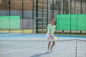 Portrait of a sporty woman with a racket in her hands playing tennis on the court and looking away with a serious face. Tennis concept.