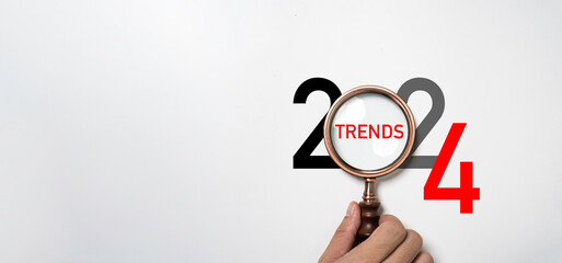 Hand holding magnifier glass with 2024 year and trends wording for focusing 2024 business marketing trends and planing change concept.