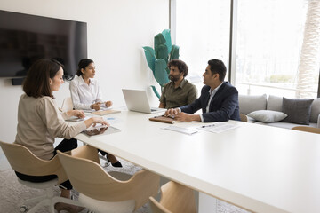 Young Indian business coach woman holding brainstorming meeting with diverse employees, giving...