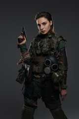 Portrait of a female soldier in military uniform with a pistol, embodying a rebel or partisan in a Middle Eastern conflict against a gray backdrop