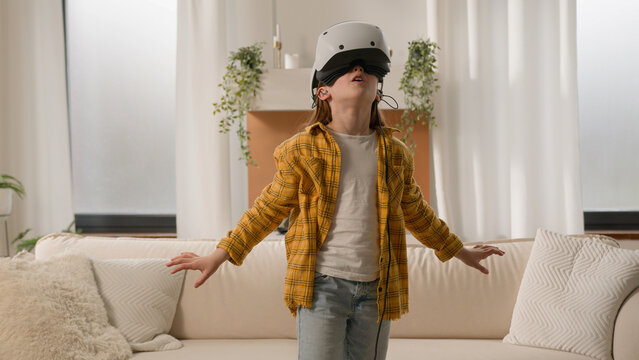 Funny happy kid girl playing online video 3d game using virtual reality headset child schoolgirl play in vr glasses at home in living room explore cyberspace world metaverse innovative technology AR