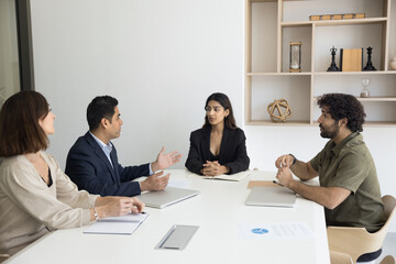 Multiethnic business partners discussing partnership, investment to startup, discussing agreement. Pretty young Indian businesswoman holding brainstorming meeting with employees
