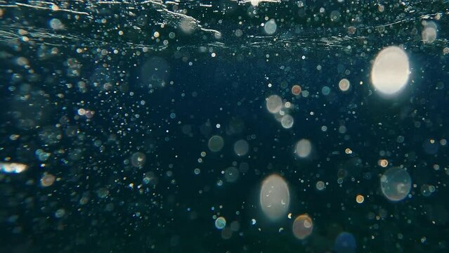Air bubbles and glare of evening sun on surface of water at sunset time, underwater shot