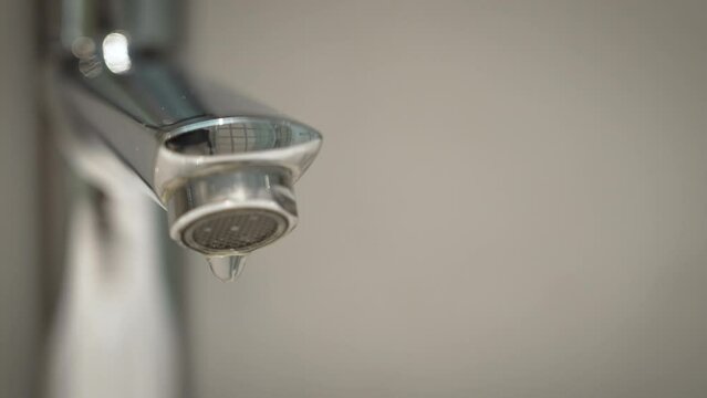 Water drops dripping from the bathroom faucet tap. Water leaking. Slow motion