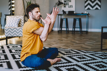 Calm young man practicing asana during sportive exercises in apartment