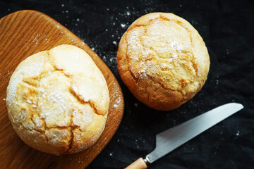 Freshly baked scones on a board next to a jar of jam and a knife on a dark background