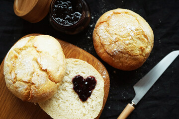 Freshly baked scones on a board next to a jar of jam and a knife on a dark background