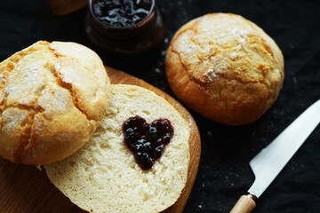 Freshly baked scones on a board next to a jar of jam and a knife on a dark background