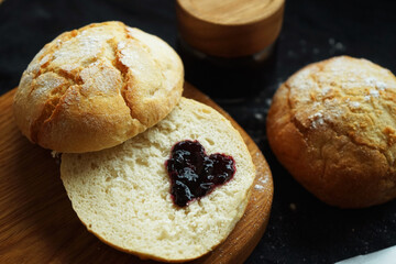Freshly baked scones on a board next to a jar of jam and a knife on a dark background