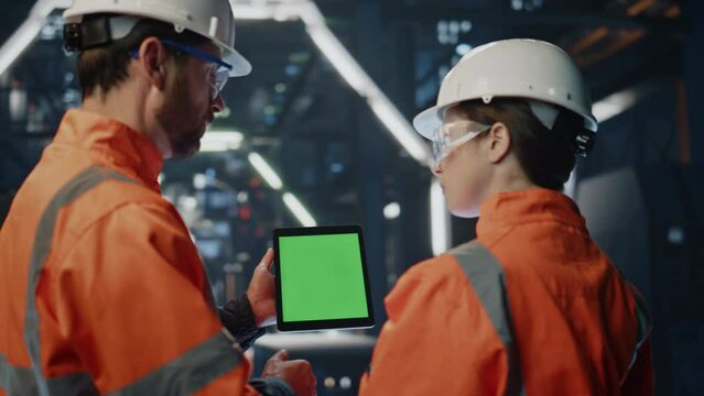 Two engineers looking mockup tablet discussing technical data on factory closeup