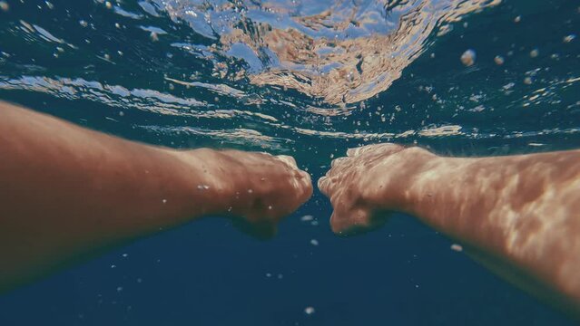 POV shot, split level, guy paddling with his hands underwater to rocky shore