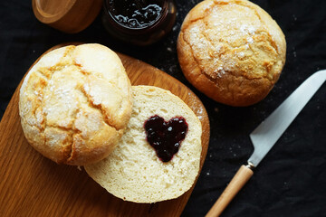Freshly baked scones on a board next to a jar of jam and a knife on a dark background