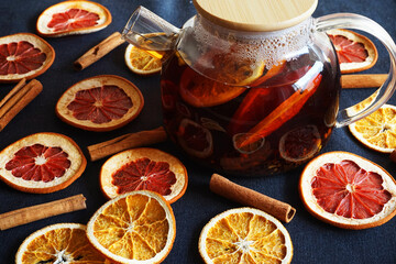 Glass teapot with black tea with orange next to dried orange and grapefruit slices on a dark background