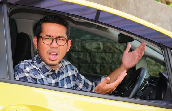 Adult Asian man sitting inside a car and showing confuse expression