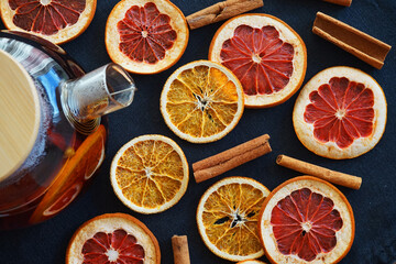 Glass teapot with black tea with orange next to dried orange and grapefruit slices on a dark...