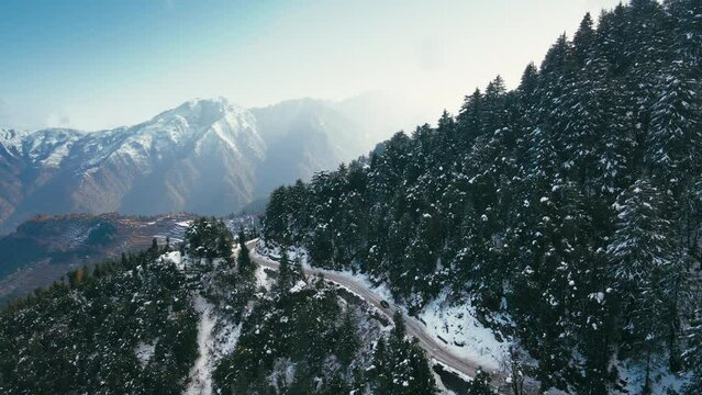 Aerial view of beautiful hilly roads covered with snow during winters in the Himalayan region of Uttarakhand. Snow-covered trees and cars moving on steep mountain roads. A dro following a car in hills