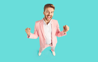 Happy guy celebrating his success and having fun. High angle shot of joyful young man in pink suit...