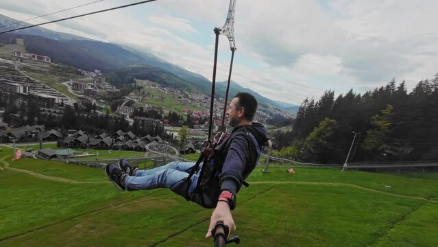 A man goes down a zip line and films himself with a selfie stick.