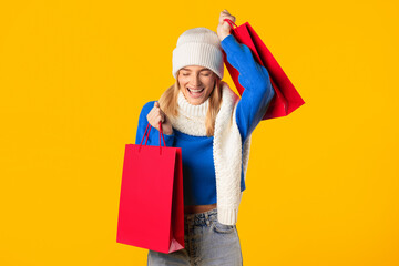 Excited woman with red shopping bags on a yellow background
