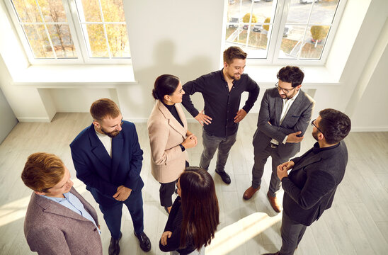 Different People Meeting And Communicating At A Modern Business Event. Group Of Happy Young Men And Women Standing In The Office And Talking. Communication Concept. High Angle Shot, Overhead View