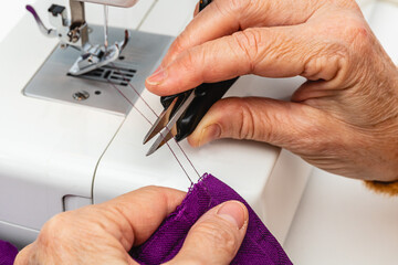 Horizontal photo hands of adult mature woman seamstress cutting thread. Concept hobbies, handicrafts