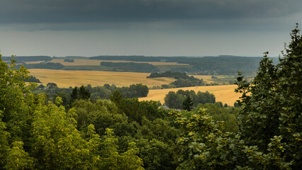 view from the hillside to the hilly agricultural fields under a cloudy sky. summer august rural landscape