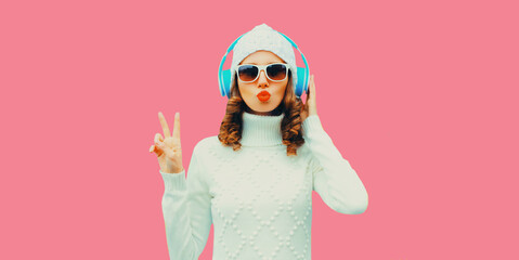 Winter portrait of stylish modern woman in wireless headphones listening to music wearing white...