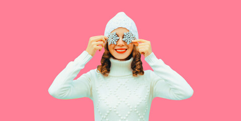 Winter portrait of happy smiling woman holding snowflakes covering her eyes wearing white knitted...