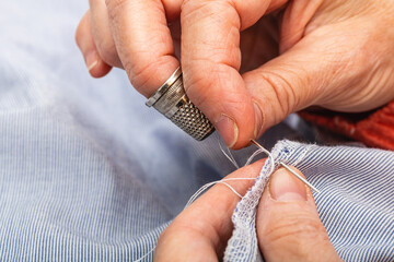 Close up photo extreme horizontal, hands mature adult woman. sewing with needle. Concept tailor