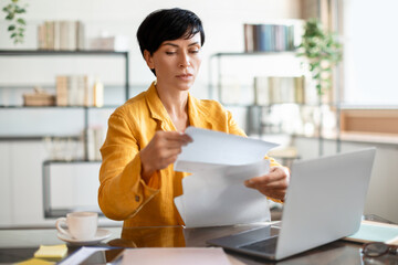 Focused middle aged woman entrepreneur reviewing documents at office workspace