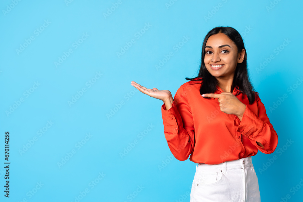 Wall mural Happy arabic woman pointing at copy space over blue background