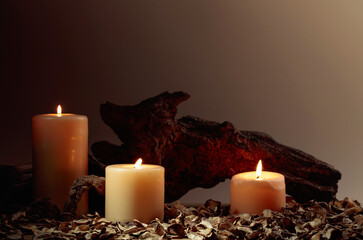 Burning candles and old wooden snags on a brown background.