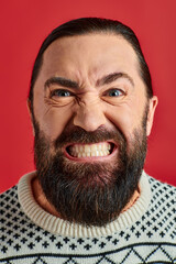 bearded man in winter sweater with ornament grinning on red background, Christmas and New Year