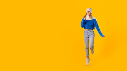 Fototapeta na wymiar Joyful woman in winter clothes jumping on yellow background, indicating shopping deals