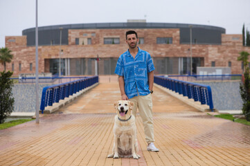 Handsome young bearded man and his large dog stop for a rest. The dog is a brown Labrador retriever. Concept pets and companion animals. International dog day.