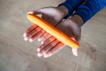 The woman holds food in her hand. the girl holds carrots in her hands. Orange carrot in hand