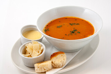 Fresh tomato soup in a bowl with bread, cream and parmesan cheese.