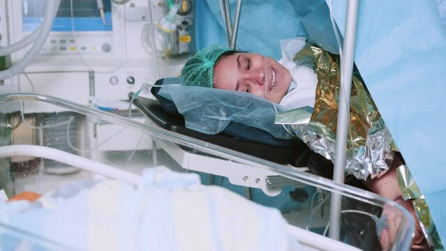 Mother Holds Newborn Baby in Hospital. Mother Holding Her Newborn Baby on Her Chest Just After Delivery. First Sight of Mom and Her Newborn in Operation Room. Modern Hospital Operation Room