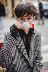 A young girl in a coat with short black hair sits in a cafe with a cup of coffee. Outdoor autumn