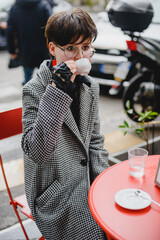 A young girl in a coat with short black hair sits in a cafe with a cup of coffee. Outdoor autumn